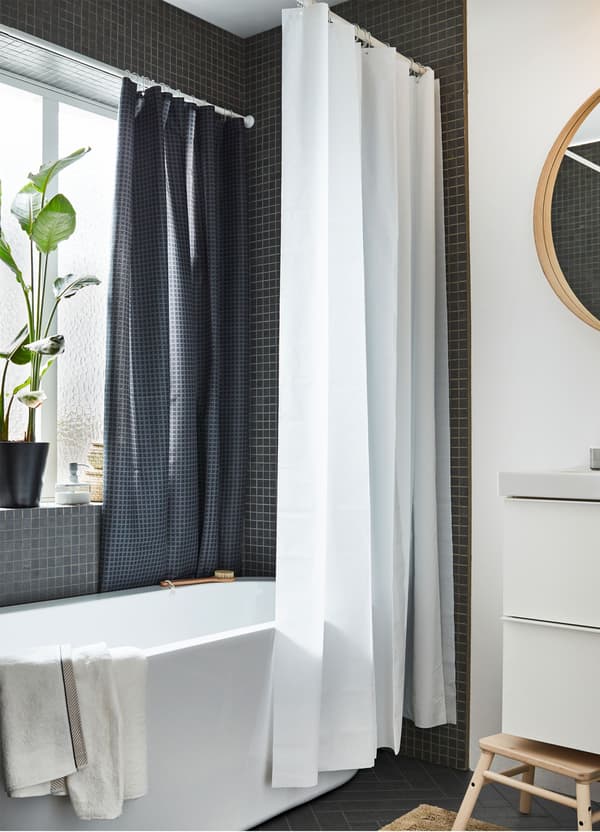 A bath surrounded by an IKEA EGGEGRUND white shower curtain and SAXÄLVEN anthracite dark grey shower curtain.