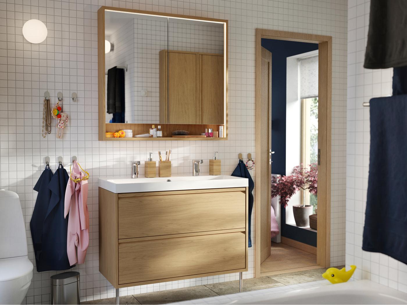 A bathroom features an ÄNGSJÖN wash-stand in oak effect with legs and a FAXÄLVEN mirror cabinet with built-in lighting.