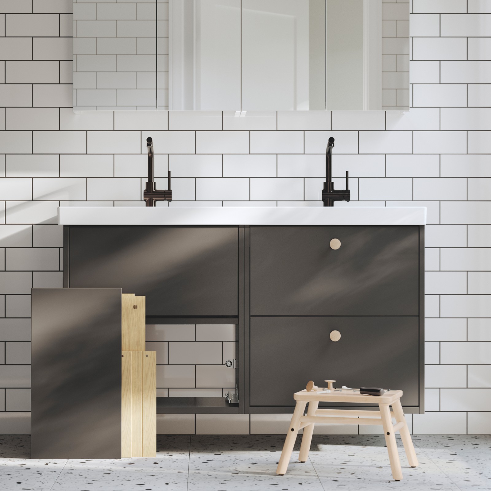 A bathroom has two dark grey HAVBÄCK vanities, one finished and one being assembled, and there are tools on a stool.