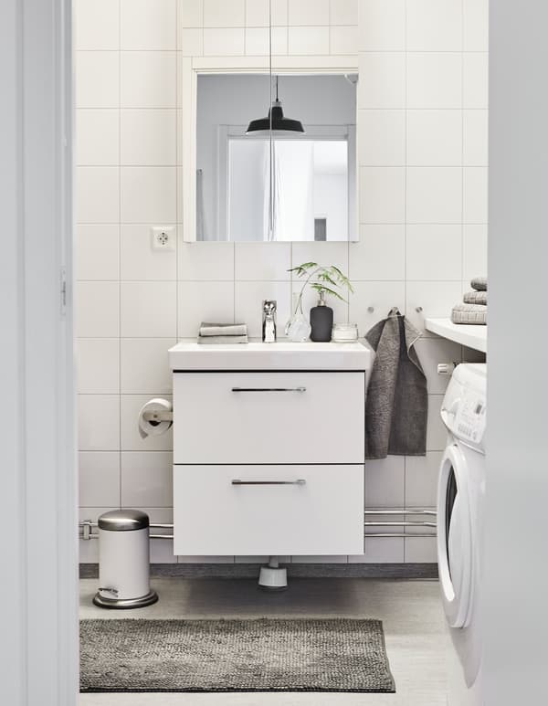 A bathroom is decorated in a white and grey palette, with fresh towels and a couple small plants.