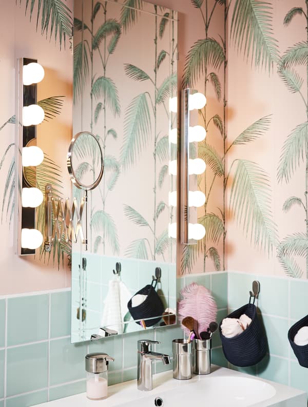 A bathroom mirror and vertical lighting on both sides of it in a green/pink bathroom.