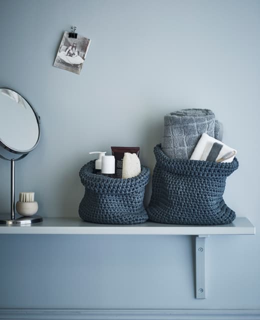 A bathroom shelf with toiletries and towels stacked in textile baskets