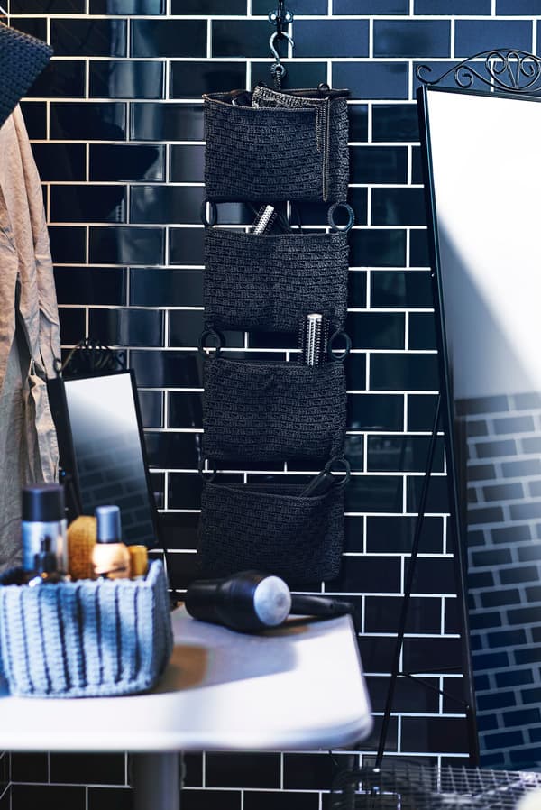 A bathroom wall organiser with hair products, hanging on a black tiled wall.