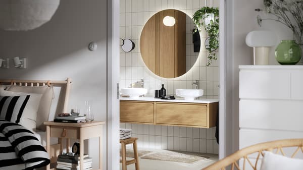 A bathroom with a circular mirror, two white sinks, a wooden vanity unit, and a hanging plant.