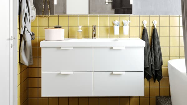 A bathroom with a GODMORGON wash-stand with four drawers, various items on it, and a mirror above it.
