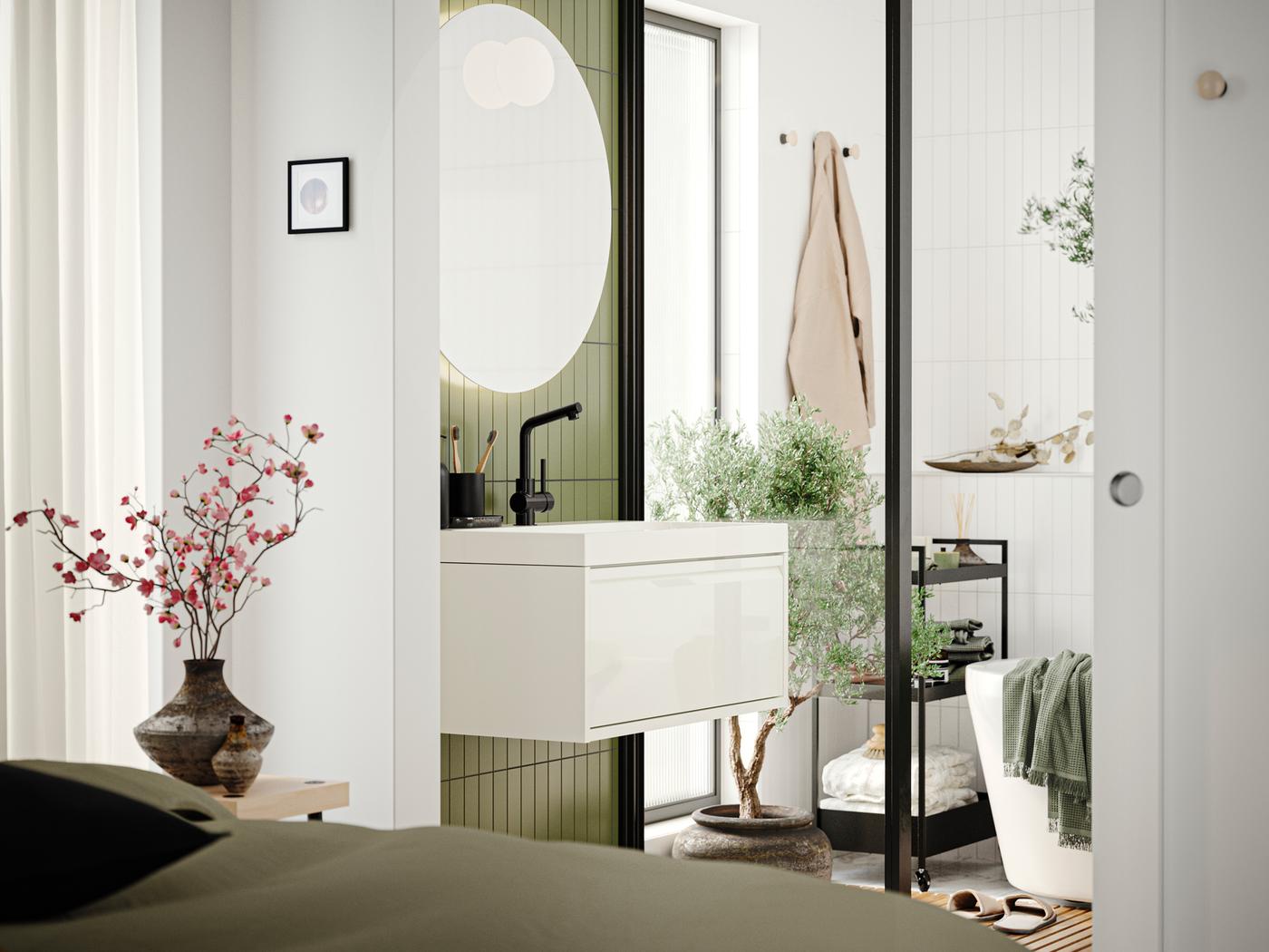 A bathroom with an ÄNGSJÖN sink cabinet with drawer in high-gloss white, a mirror and a bathtub seen from a bedroom.