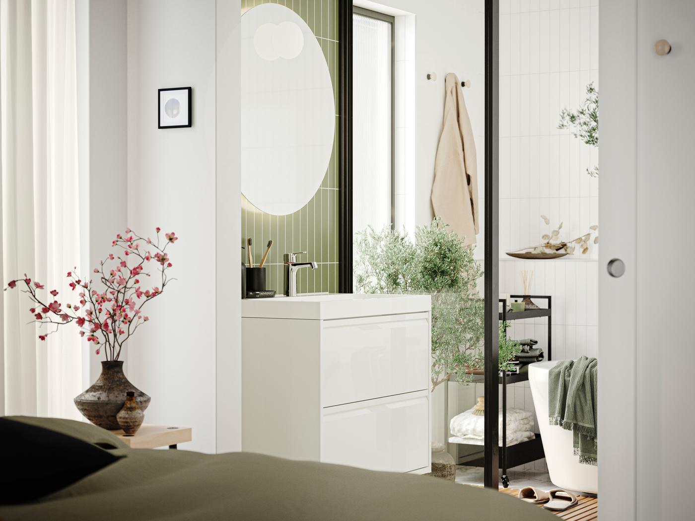 A bathroom with an ÄNGSJÖN wash-stand with drawer in high-gloss white, a mirror and a bathtub seen from a bedroom.