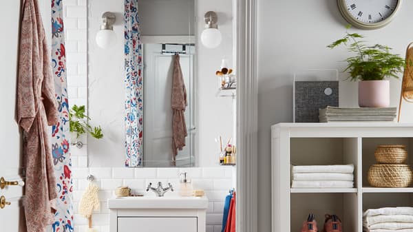 A bathroom with an EIDSÅ mirror, two FRIHULT white wall lamps, a storage unit with towels, sneakers and rattan baskets.