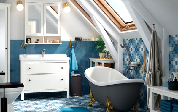 A bathroom with blue floor and wall tiles, a free-standing bath tub, and white vanity unit with mirrored cupboards above.