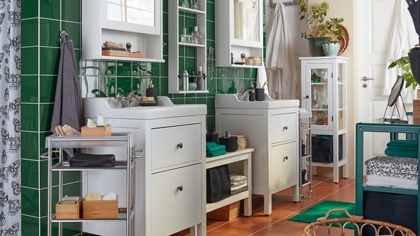 A bathroom with green tiles, two white HEMNES wash-basins and mirror cabinets, towels and accessories on display.