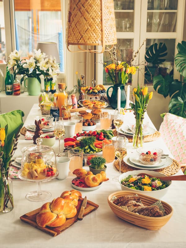 A beautifully set dining table with various foods, flowers in vases, and a cozy, sunlit room in the background.