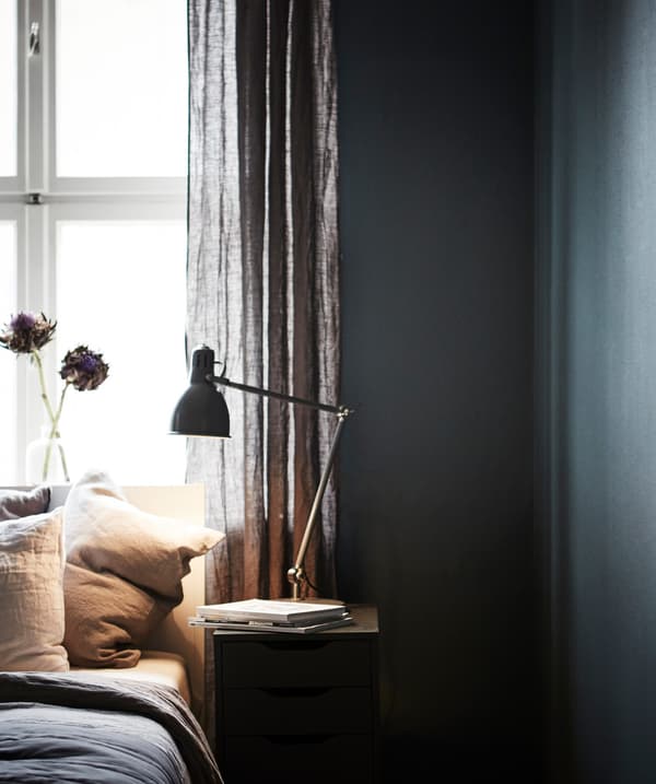  A bed and bedside table in front of a window in a bedroom painted dark blue/green.