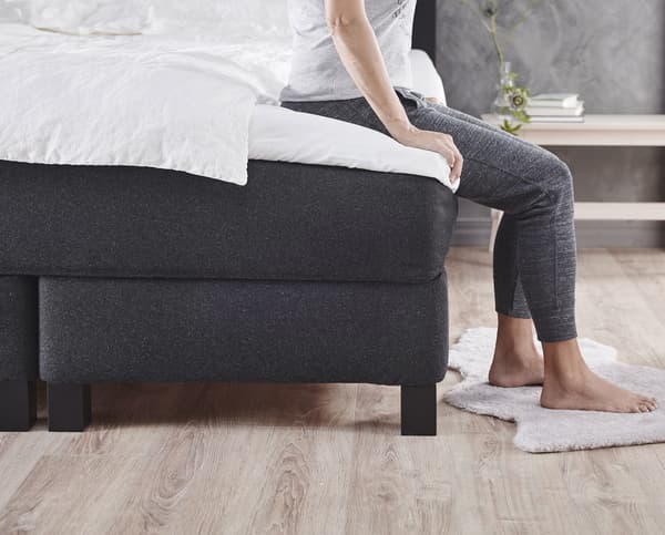 A bed base with mattress on top that a person is sitting on.