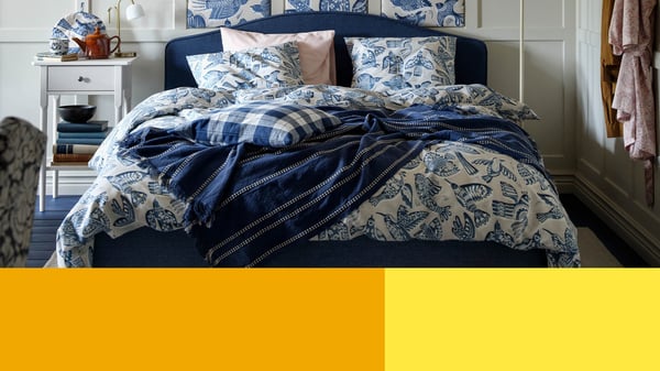 A bed dressed with a blue floral duvet cover and dark blue blankets