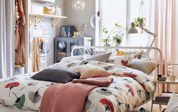 A bed dressed with floral bedding in the middle of a room with storage and shelves along the walls.