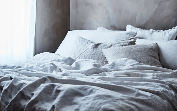 A bed dressed with layers of grey and white bedding.