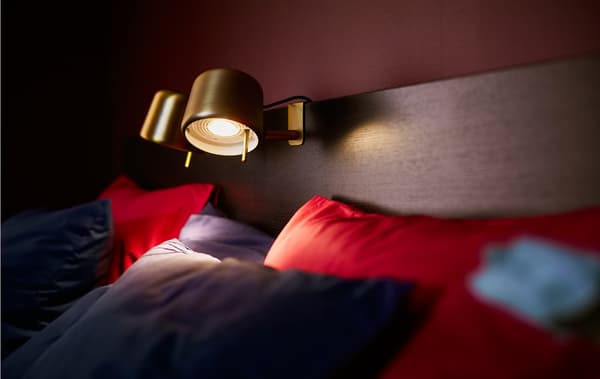 A bed in a cosy bedroom is lit with reading lamps in the centre of the headboard.