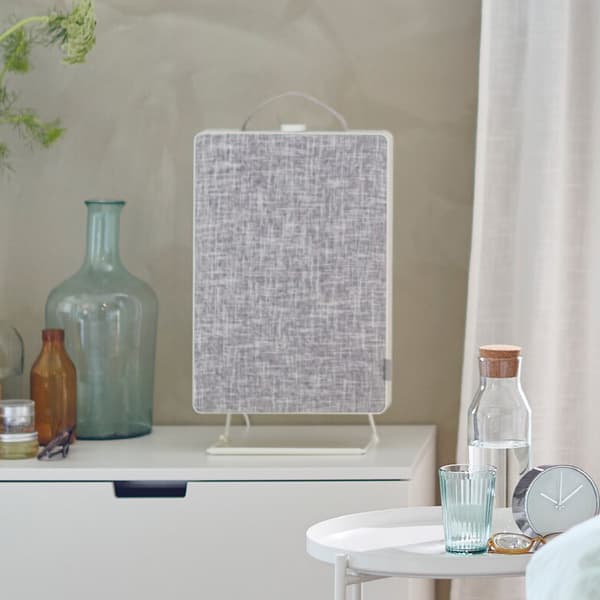 A bed in front of a window and next to a chest of drawers with a FÖRNUFTIG air purifier on top.