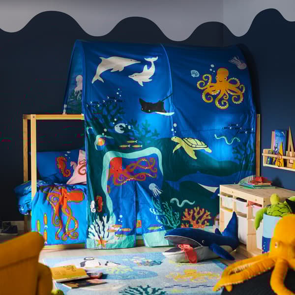 A bed is covered in a KURA ocean animals bed tent; a BLÅVINGAD blue whale soft toy is on a BLÅVINGAD rug in front of it.
