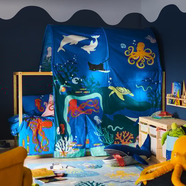 A bed is covered in a KURA ocean animals bed tent; a BLÅVINGAD blue whale soft toy is on a BLÅVINGAD rug in front of it.