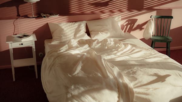 A bed is half-made with the white DYTÅG duvet cover in a pink bedroom; the duvet cover and pillows are softly rumpled.