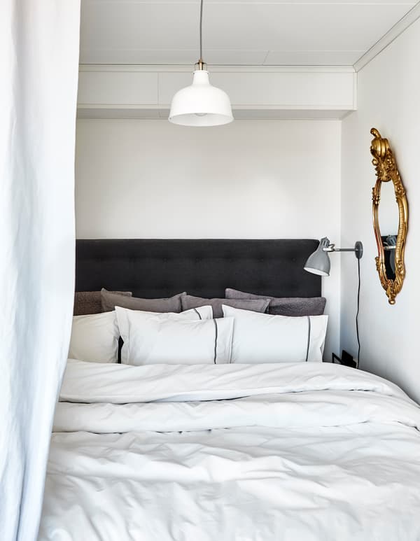 A bed is made up with lots of fluffy pillows and thick comforters in neutral shades.