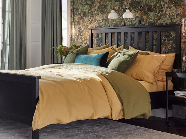 A bed made up with PUDERVIVA quilt covers and pillowcases in yellow and green, a yellow sheet and a cushion in green velvet.