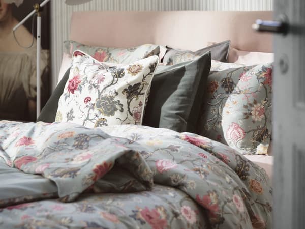 A bed made with a floral pink and light green duvet cover and pillows to match.
