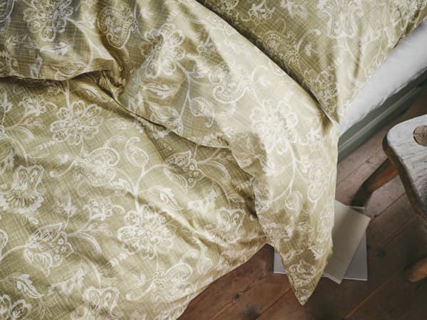 A bed made with IKEA JUNIMAGNOLIA bed linen in cotton with a classic, white and green flower print.