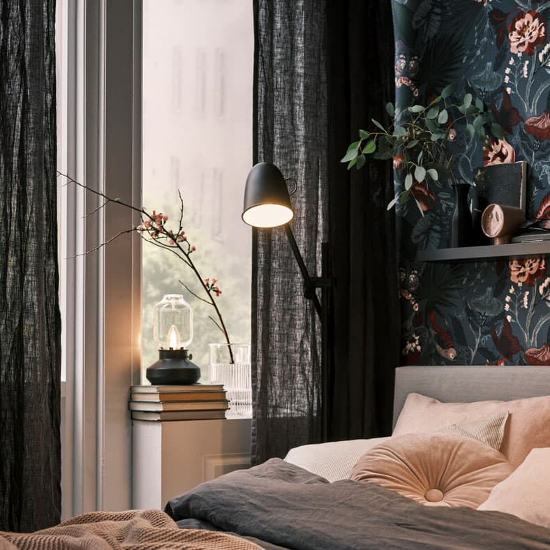A bed on a dark, floral wall, with black SKURUP floor/reading lamps on both sides, plus a TÄRNABY table lamp in a window.