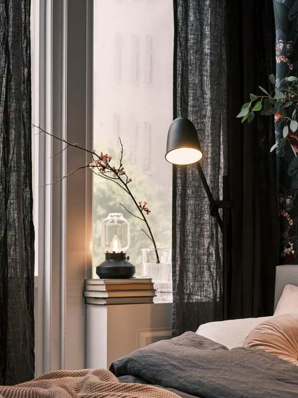 A bed on a dark, floral wall, with black SKURUP floor/reading lamps on both sides, plus a TÄRNABY table lamp in a window.