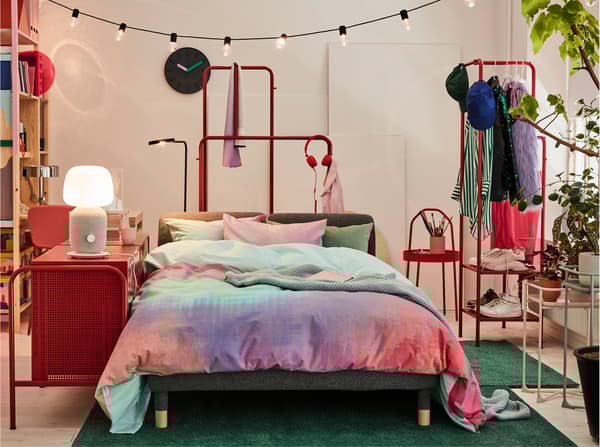 A bed sofa that's turned into a bed and filled with colorful bed textiles and a chest of drawers that serve as a nightstand.