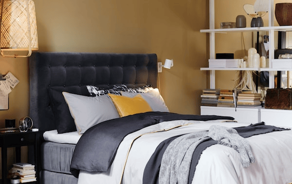 A bed with a grey velvet quilted headboard and layered bedlinen.