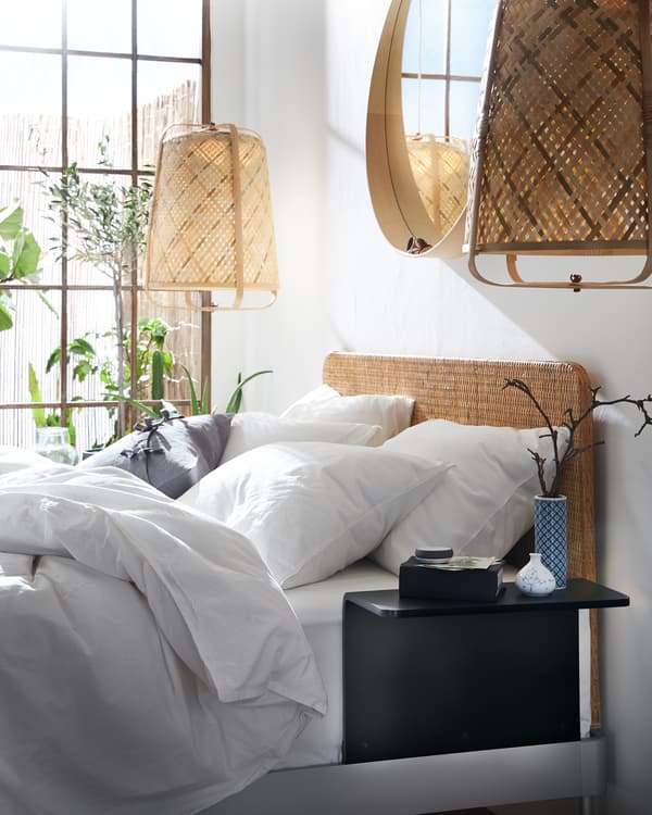 A bed with a rattan headboard and a white quilt cover and pillowcases. Pendant lamps in bamboo hang on each side of the bed.