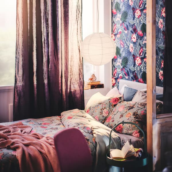A bed with a throw and bed linen dressed in a NÄSSELKLOCKA duvet cover and pillowcase set, with a pendant lampshade above.