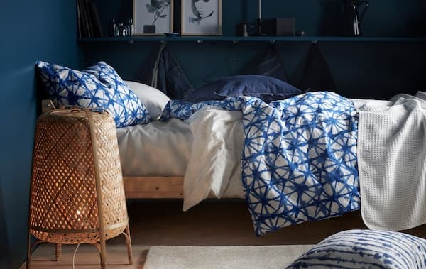 A bed with blue and white patterned bedding and a bamboo floor lamp in a room with dark blue walls.