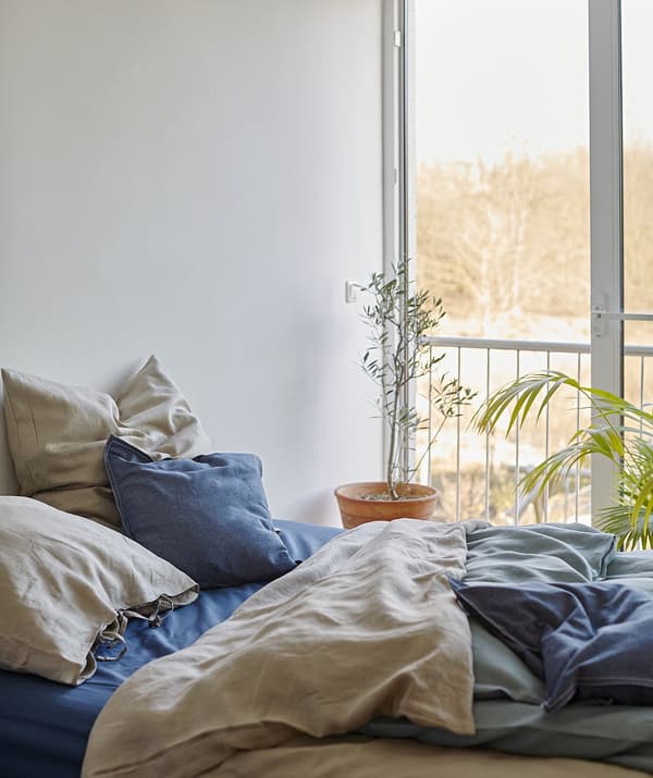 A bed with layered bedding in blue and beige next to a large window.