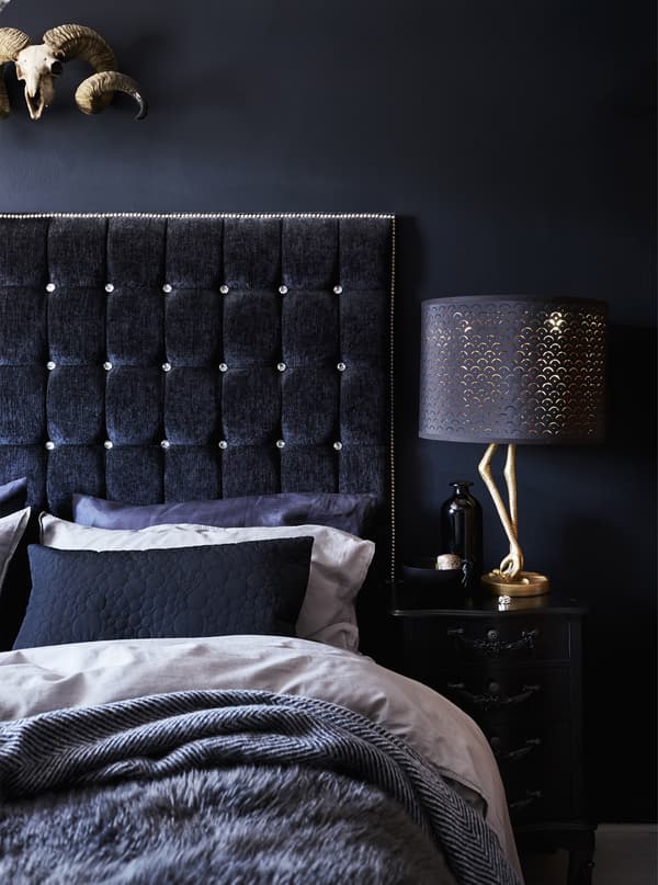 A bed with layers of cosy textiles in black and grey and a black velvet headboard with button tufting.