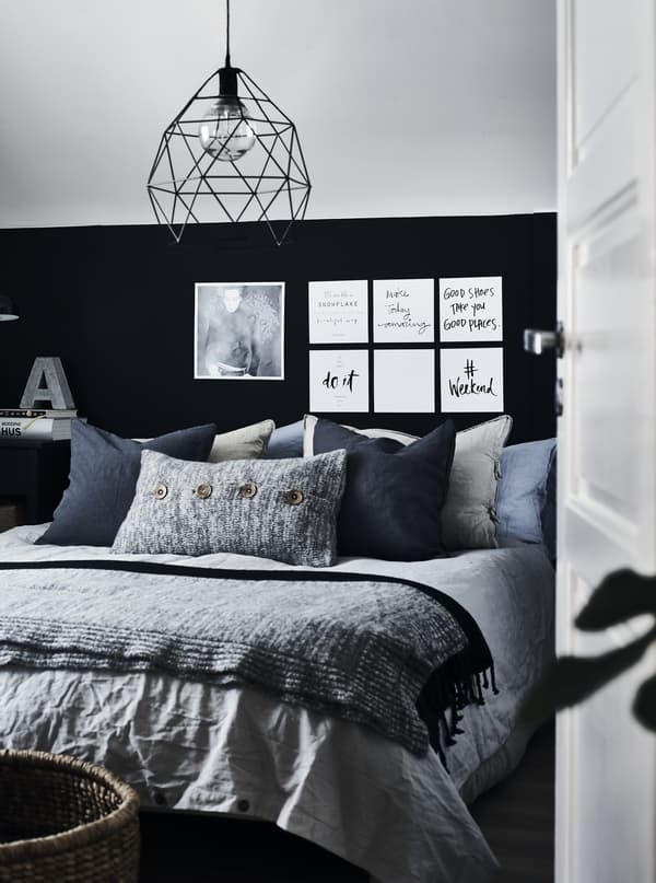 A bed with lots of cushions in different sizes, material and grey colours against a black and grey wall.