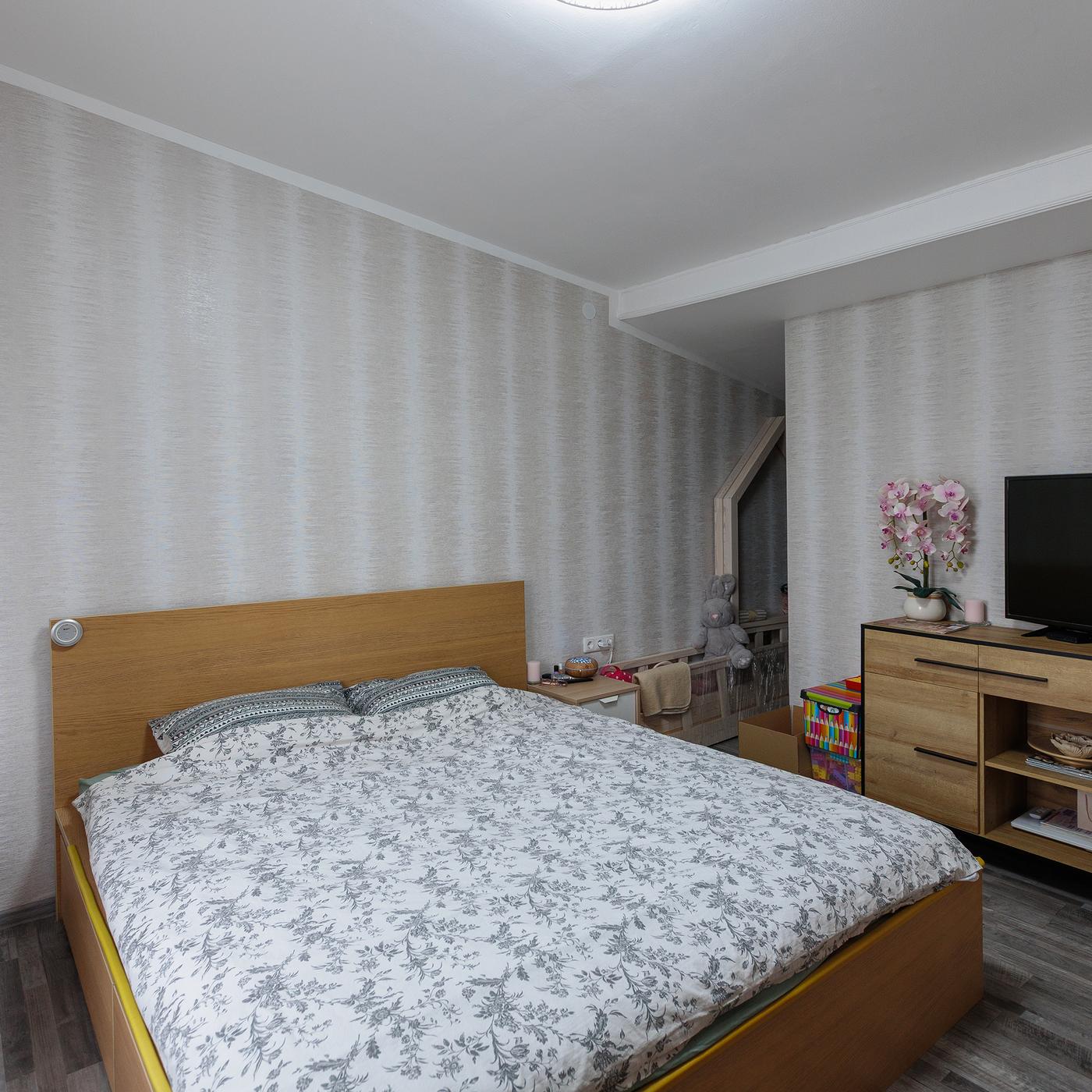 A bedroom before the makeover, featuring a wooden bed with a patterned duvet and a TV on a wooden cabinet against the wall.