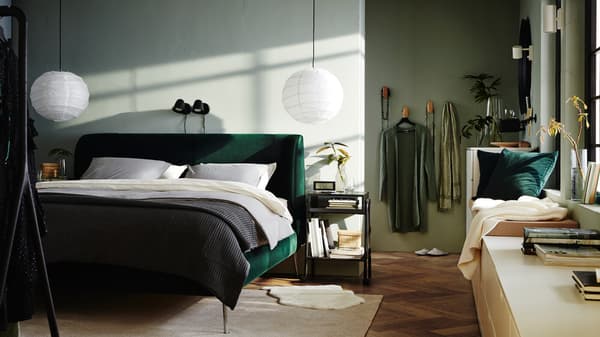 A bedroom containing a green TUFJORD bed with REGOLIT lampshades above and NORDLI drawer units with books by the windows.