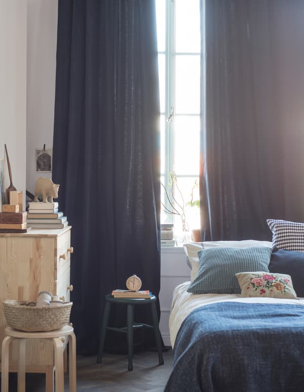 A bedroom is decorated with textiles in shades of blue and white, with curtains that hang from the ceiling to the floor.