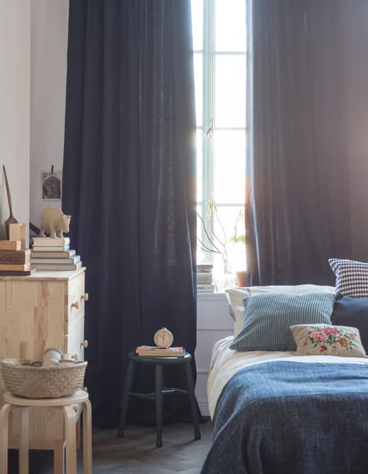 A bedroom is decorated with textiles in shades of blue and white, with curtains that hang from the ceiling to the floor.