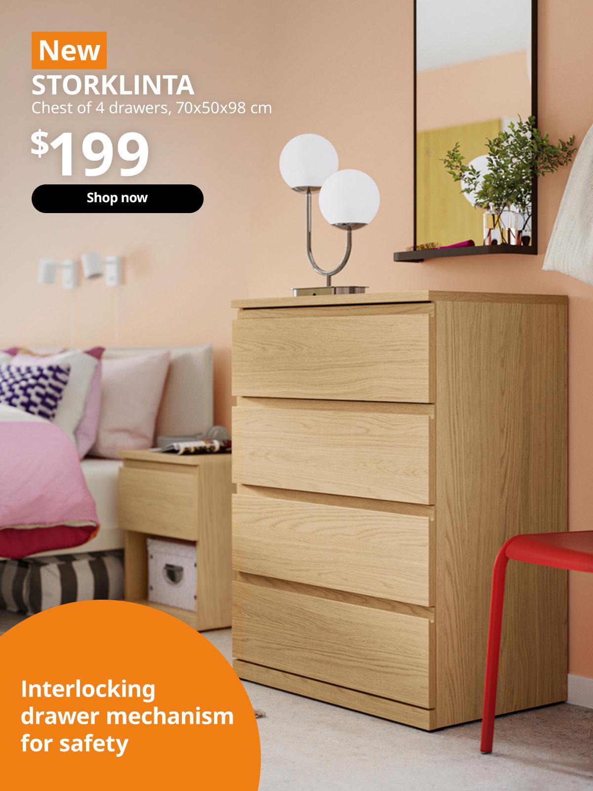 A bedroom setting lifestyle image showcasing oak effect STORKLINTA chest of 4 drawers next to the bed. A orange tag with white text that reads 'New', followed by white text overlaying image that reads 'STORKLINTA, Chest of 4 drawers, 70x50x98 cm, $199'. On the bottom left, a orange tag with white text that reads 'Interlocking drawer mechanism for safety'.