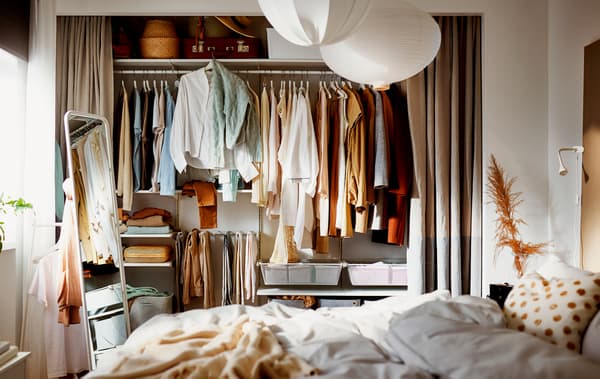 A bedroom where a wall-wide alcove has its curtains open, revealing a filled wardrobe built on a BOAXEL storage combination.