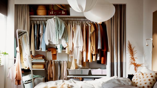 A bedroom where a wall-wide alcove has its curtains open, revealing a filled wardrobe built on a BOAXEL storage combination.