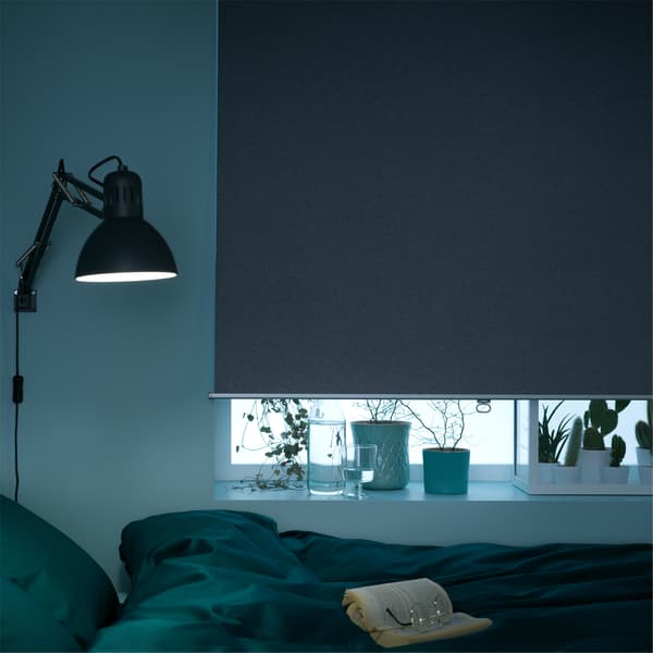  A bedroom window that's almost completely covered by a grey block-out roller blind.