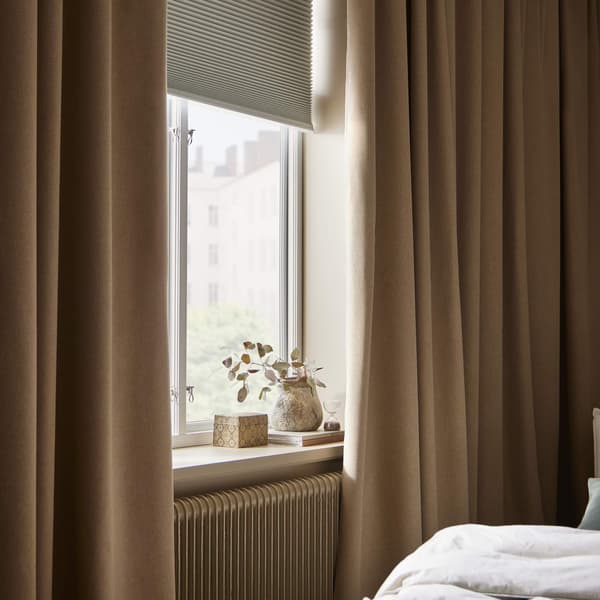 A bedroom window with dark curtains alongside of it and a blackout blind partially opened.