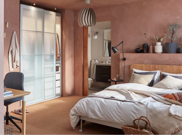 A bedroom with a bed frame in aluminum and a rattan headboard, wardrobe with frosted glass doors and a beige pendant lamp.