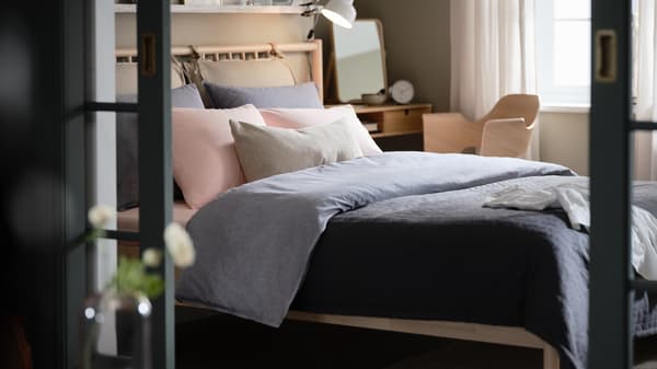 A bedroom with a BJÖRKSNÄS birch bed, dark-blue KOPPARBLAD bed linen, a NORDKISA dressing table, and a FJÄLLBERGET chair.